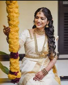 a woman sitting on the ground next to a pole with flowers in her hair and wearing a white saree