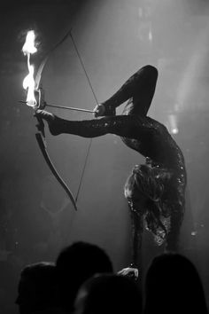 a woman is performing with an arrow on stage