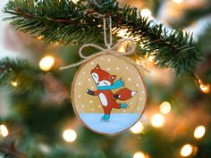 a christmas ornament hanging from a tree with lights in the background and an ornament shaped like a fox on it