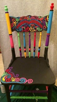 a chair made out of wooden sticks with colorful designs on it, sitting in front of a wall