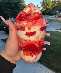 a person holding up a plastic cup filled with ice cream and strawberries on top