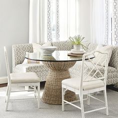 a glass table with chairs around it in front of a white couch and window curtain