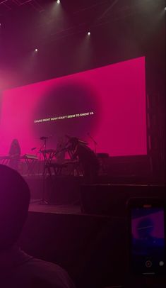 the stage is lit up with bright pink and purple lights, while people are seated in front of it