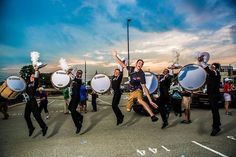 a group of people in black shirts and tan pants are holding drums while dancing on the street