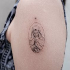 a woman's back shoulder with a small tattoo of a praying person on it