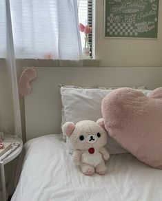 a white teddy bear sitting on top of a bed next to a pink heart pillow