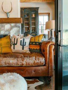 a brown leather couch sitting in a living room next to a lamp and table with two pillows on top of it