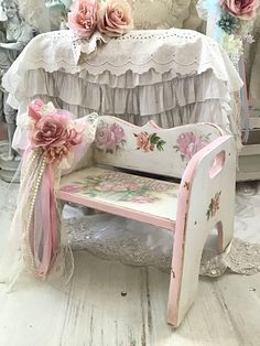 a white bench with pink flowers on it in front of a bed and table cloths