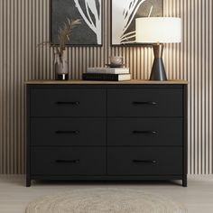 a black dresser sitting next to a lamp on top of a wooden table in front of a striped wall