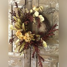 a wreath is hanging on the door with flowers and leaves around it in front of an old wooden door