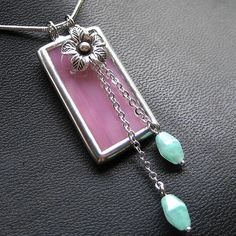 a necklace with pink and green beads hanging from it's side on a black surface