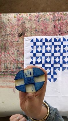 a woman holding up a piece of art with blue and white designs on the wall behind her