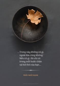 a black bowl with a leaf in it on top of a gray table next to a quote