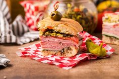 a sandwich sitting on top of a red and white checkered napkin next to some pickles