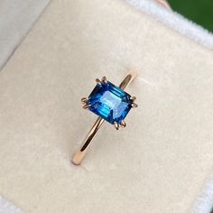 a ring with a blue topaz sits on a white cloth in a gift box