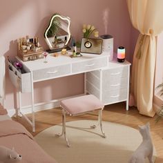 a white desk with drawers and a mirror on it in a pink room next to a cat