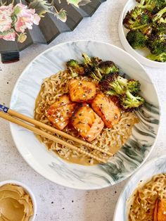 two plates with noodles, broccoli and shrimp on them next to chopsticks