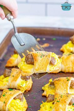 sausage and egg breakfast rolls on a baking sheet with a spatula being used to scoop them