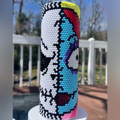 a colorful beaded can sitting on top of a white table next to a fence