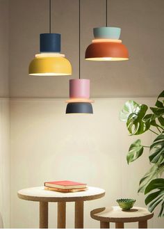 three different colored lamps hanging from the ceiling above a table and two small tables with books on them