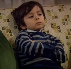 a little boy sitting on top of a couch next to a green pillow in front of him