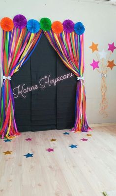 a black backdrop with colorful streamers and pom poms on the top is decorated with stars