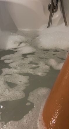 a bathtub filled with foam and water next to an orange object on the floor