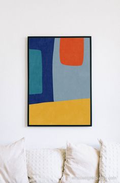 a painting hanging on the wall above a white couch with pillows and throw pillows in front of it