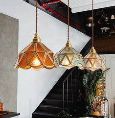 three lights hanging from the ceiling in a room with stairs and potted plants on the table