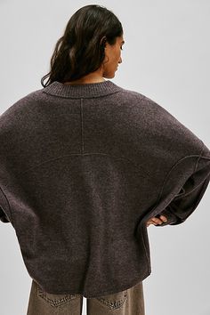 a woman standing with her back to the camera wearing a brown sweater and khaki pants