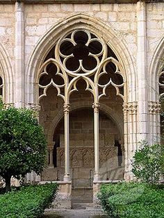 an arched window in the side of a stone building with trees and bushes around it