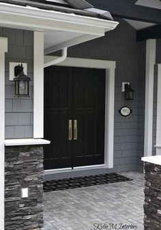 a black front door on a gray house with white trim and two lanterns above it