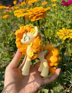 someone is holding a toy in their hand near some flowers and daisies on the ground