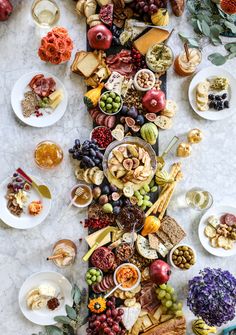 several people are sitting at a table full of food and drinks, with their hands reaching for the platter