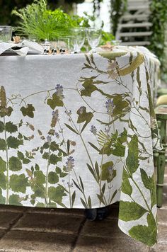 a table covered with a green and white floral design on top of a brick floor