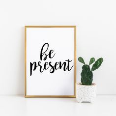 a framed poster with the words be present next to a potted cacti