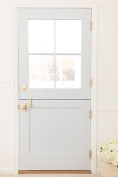 a white front door with two windows and a basket full of flowers on the floor