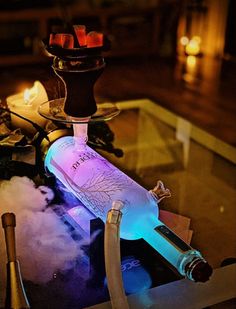 a lit up bottle sitting on top of a glass table next to candles and bottles