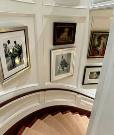 a spiral staircase with framed pictures on the wall and below it is a set of stairs