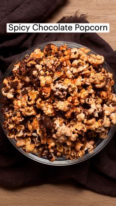 a glass bowl filled with chocolate popcorn on top of a wooden table next to a black cloth