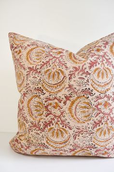 a pink and orange pillow sitting on top of a white table next to a wall