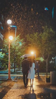 two people walking in the rain under an umbrella at night with their hands on each other's backs