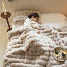 a woman laying in bed under a fluffy blanket with candles on the end table next to her