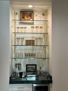 a kitchen area with glass shelves and white cupboards, black counter top and gold trim