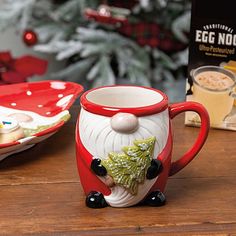 a santa clause mug sitting on top of a wooden table next to a christmas tree