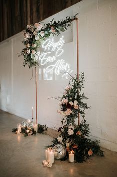 a wedding arch with candles and flowers on the floor in front of a white wall