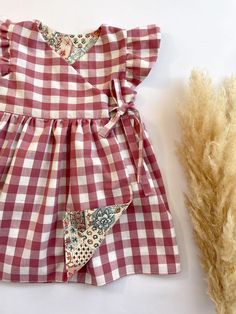 a red and white checkered dress sitting on top of a table next to dried grass