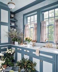 a kitchen with blue cabinets and white counter tops, flowers in vases on the window sill