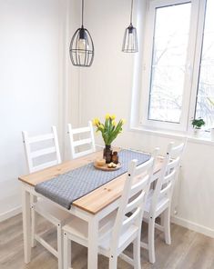 a dining room table with white chairs and yellow flowers in a vase on the table