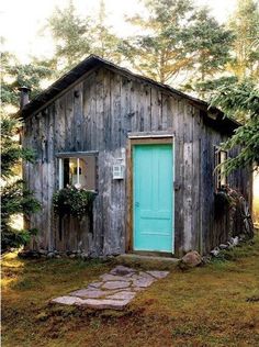 a small wooden building with a blue door in the grass next to trees and stepping stones